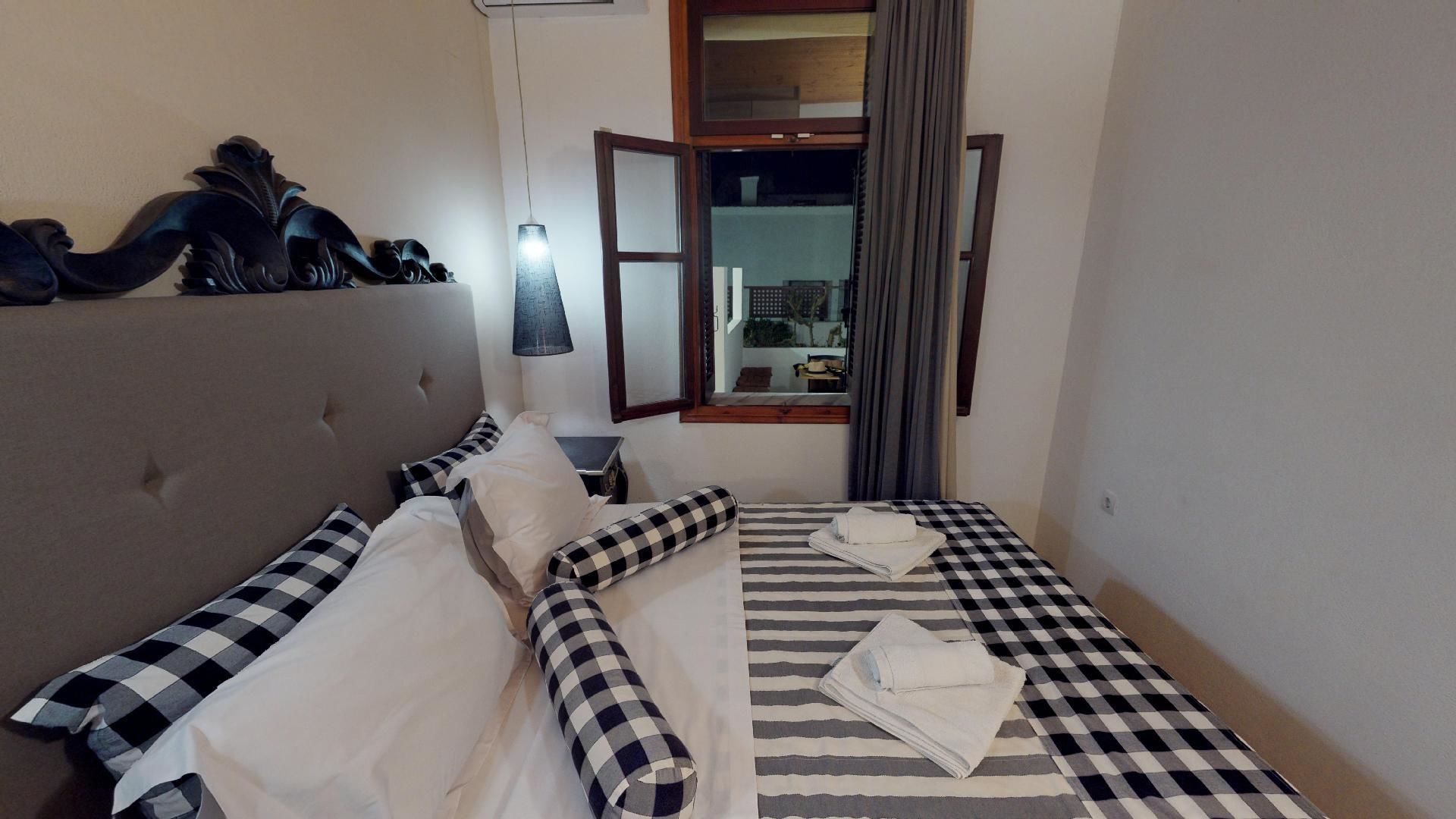 A hotel room with a bed, a headboard, a window with curtains, and a view of the outside.