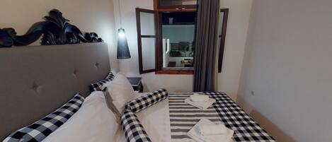 A hotel room with a bed, a headboard, a window with curtains, and a view of the outside.