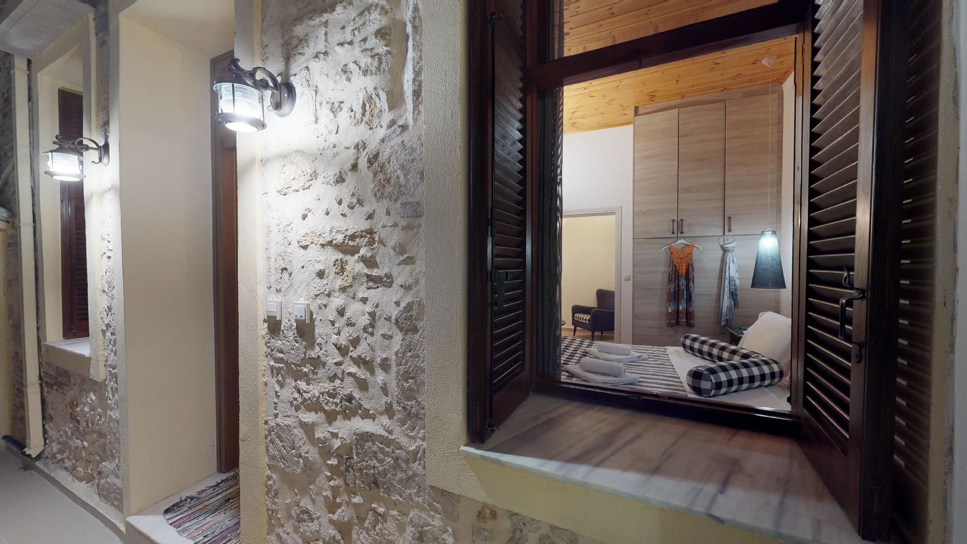 Un pasillo de hotel con pared rústica, techo de madera y una vista parcial de una habitación con cama, silla y armario.