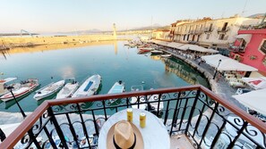 A balcony with a view of a harbor, boats, and buildings. - Porto Enetiko Suites (Rethymno)