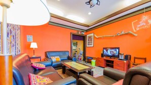 A living room with orange walls, a television, a bicycle, and a coffee table. - Oasis Inn (Hengchun)
