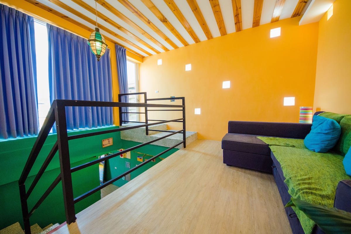 Um quarto com uma cama beliche, um sofá, um tapete verde e uma janela com cortinas azuis.
