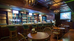 Un espace bar avec des meubles en bois, un comptoir, des étagères remplies de bouteilles et un écran diffusant un programme.