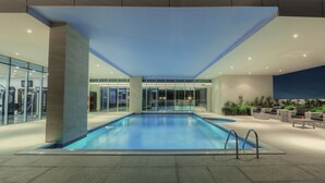 Une grande piscine intérieure aux murs de verre, dotée d’équipements de musculation et de coins salon.