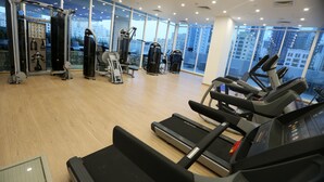 Une salle de sport équipée de tapis de course, d’appareils de musculation et dotée d’une grande fenêtre donnant sur la ville.