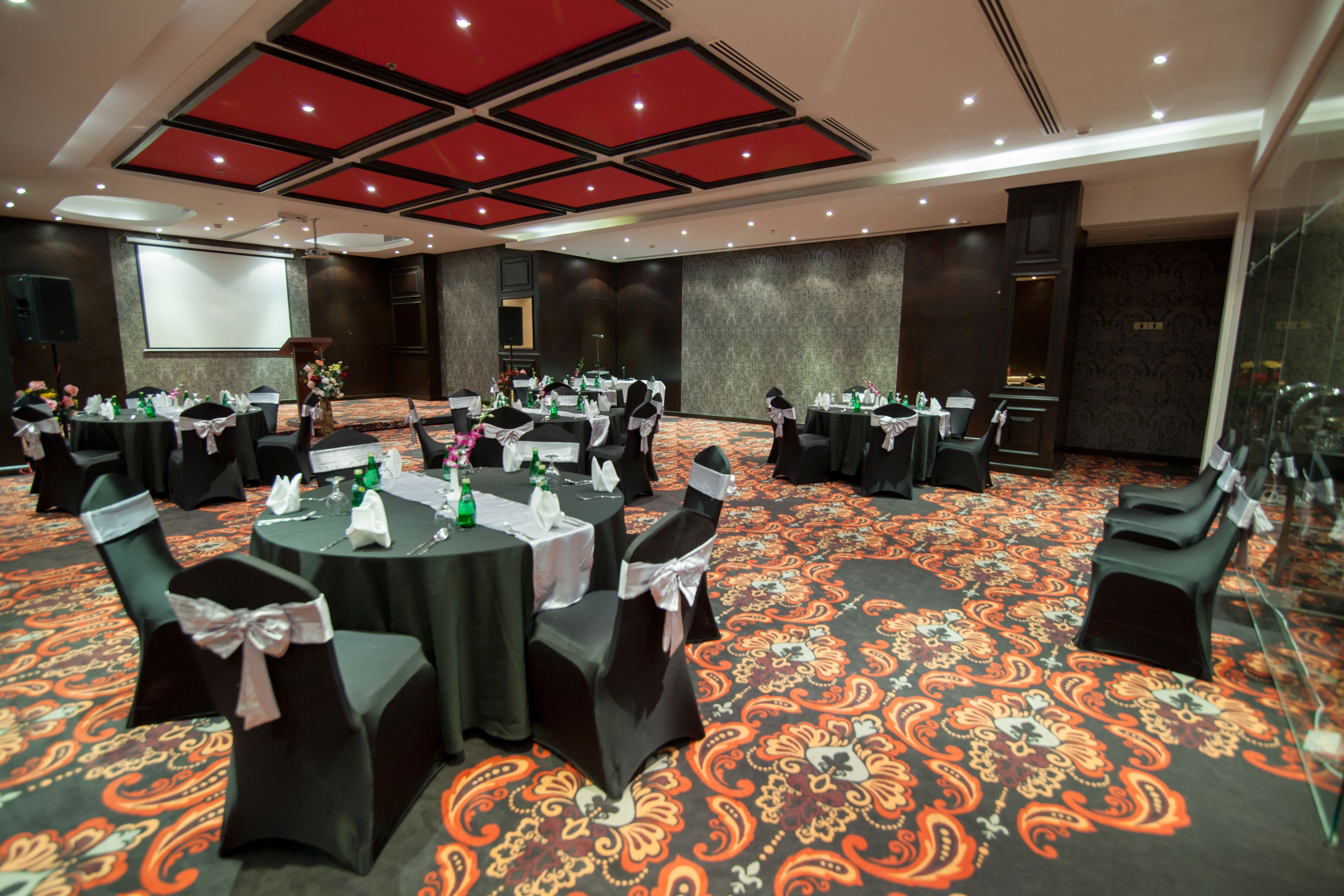 A conference room with round tables, black chairs, and a carpeted floor.