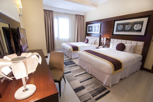 Habitación de hotel con dos camas, un escritorio, una silla, un televisor y un ventanal con cortinas.