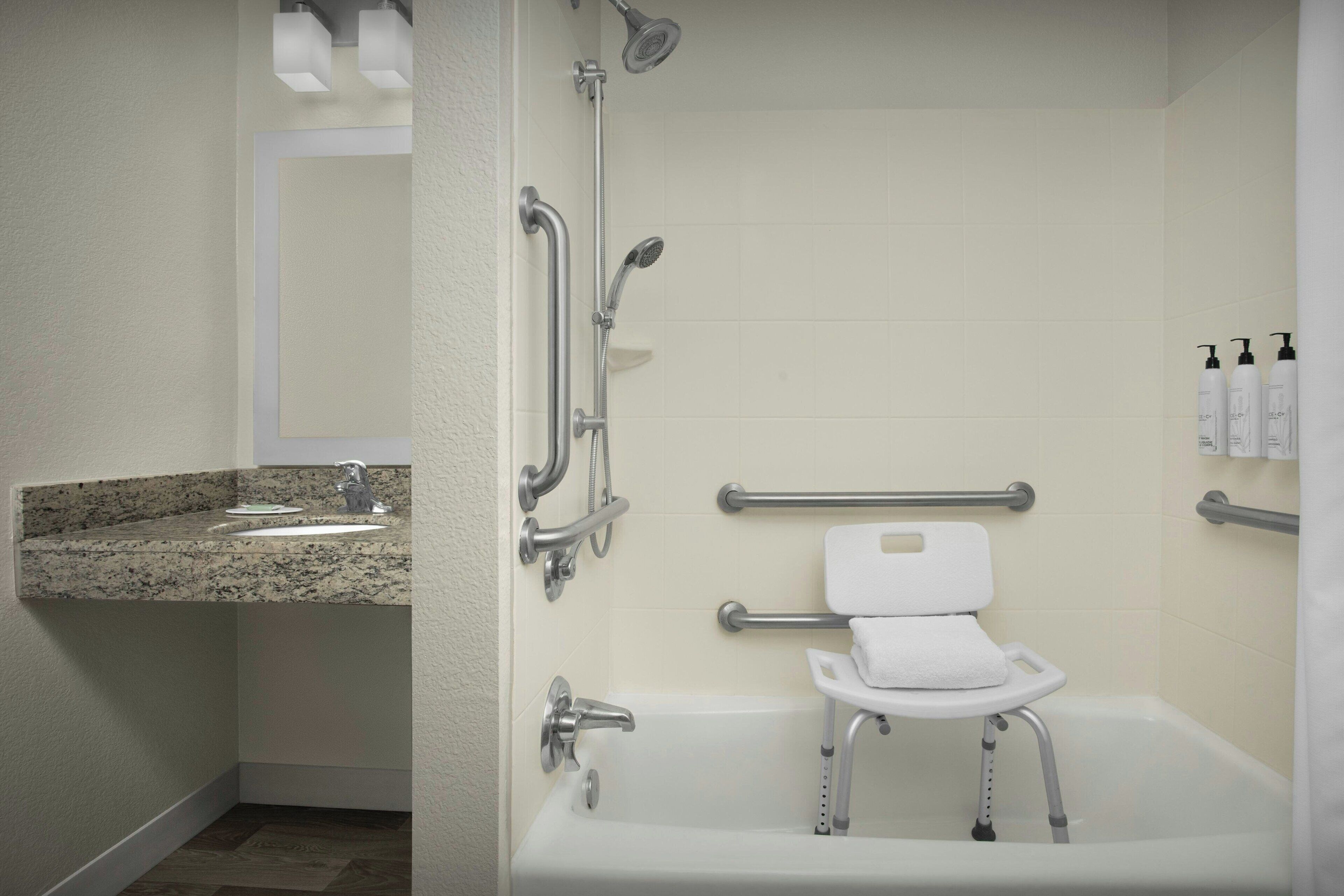 Ein Badezimmer mit Dusche, Haltegriffen, Toilette mit erhöhtem Sitz und Waschbecken.