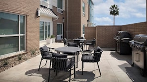 Un patio al aire libre con pared de ladrillo, una parrilla y mobiliario para exteriores.