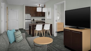 Un espacio habitable compacto con sofá, una pequeña mesa redonda, televisor, zona de cocina y una mesa de comedor con sillas.