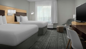 Habitación de hotel con dos camas, un escritorio con televisor, una silla, una lámpara y un ventanal con cortinas.