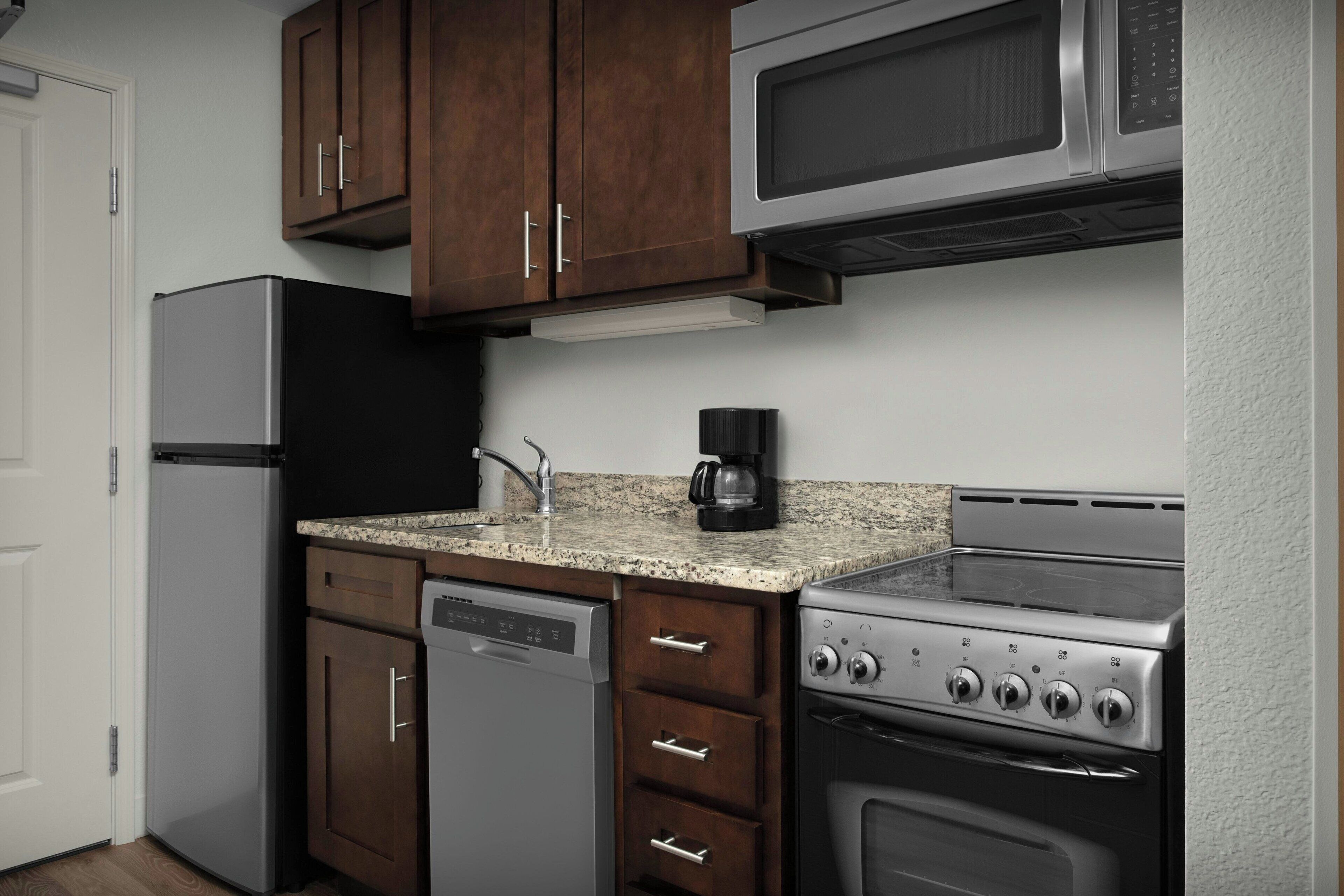 A compact kitchen with a refrigerator, microwave, coffee maker, dishwasher, and stove.