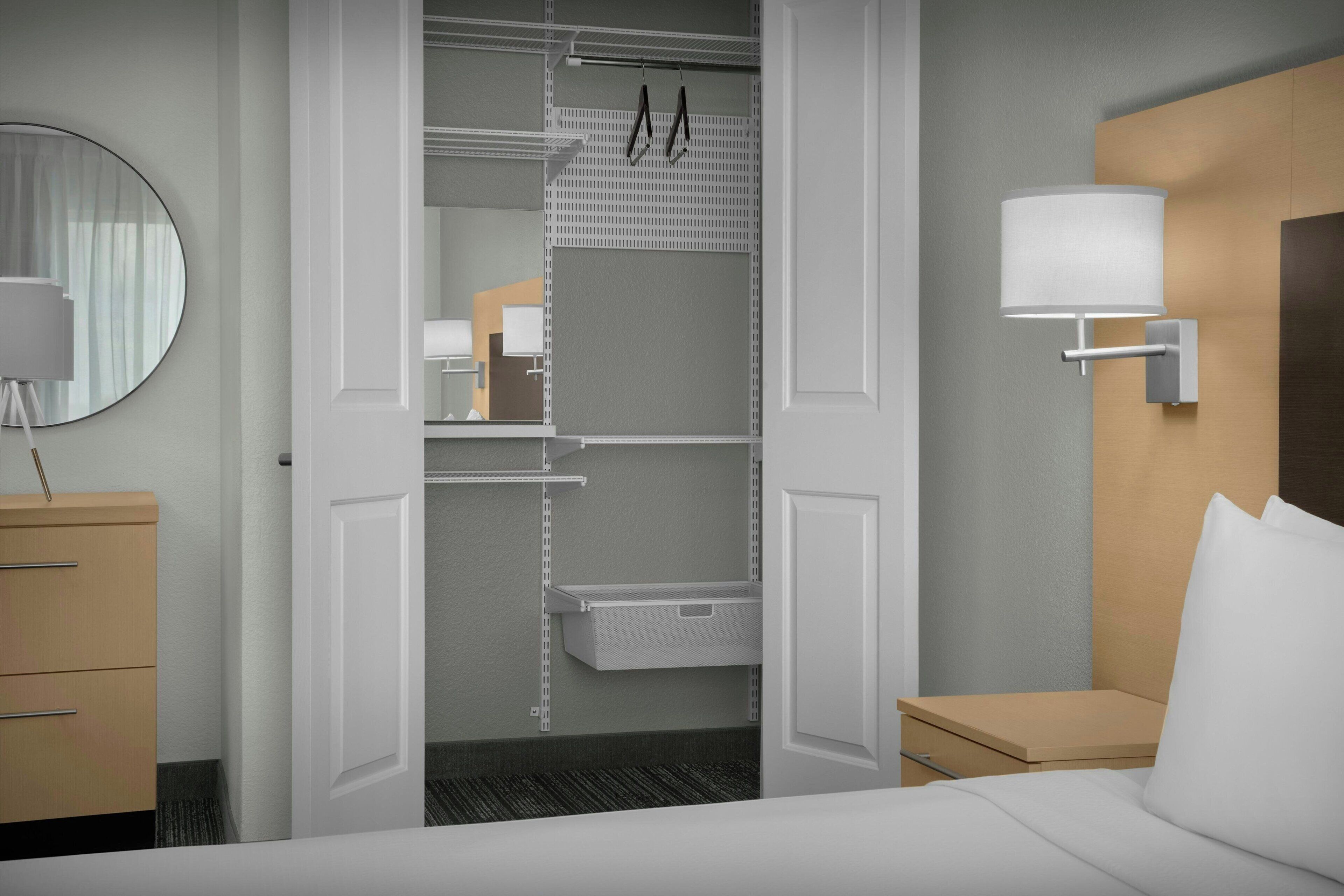 A hotel room with a bed, a bedside table, a lamp, a wardrobe, and a mirror.