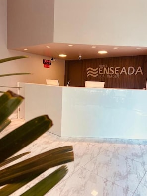 A reception desk with a digital clock and a sign for Hotel Enseada. - Hotel Enseada Boa Viagem (Recife)
