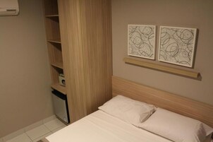 Un dormitorio con una cama, un armario de madera, un escritorio pequeño con una silla y dos cuadros abstractos en la pared.