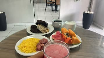 Una mesa de comedor con platos de comida, un vaso de bebida rosa y dos tazas de café.