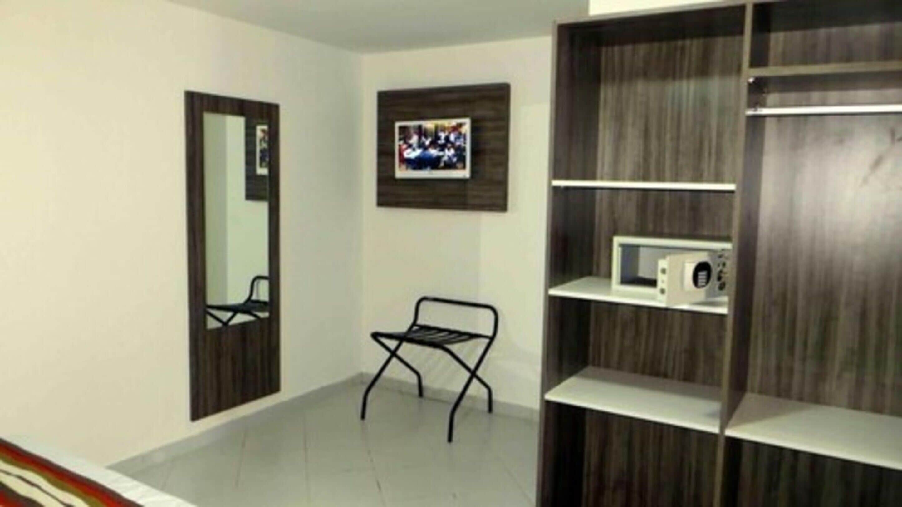Una stanza con un'armadietto in legno, un piccolo ripiano con un forno a microonde, una sedia e un quadro appeso al muro.
