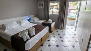 A hotel room with two beds, a small table, a window with curtains, and a view of an outdoor swimming pool. - Hotel Enseada dos Corais (Cabo de Santo Agostinho)
