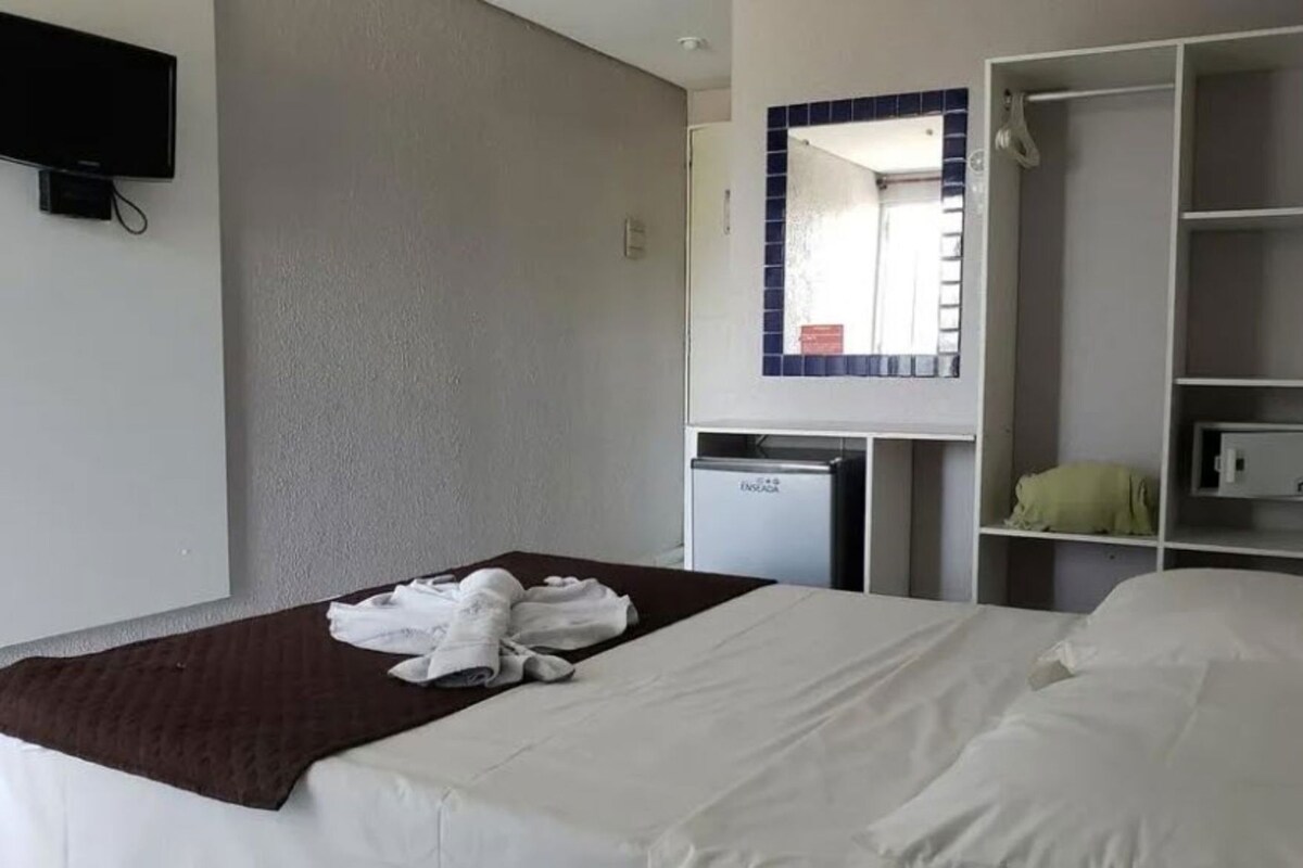 A hotel room with a bed, a small desk, a wardrobe, and a television mounted on the wall.