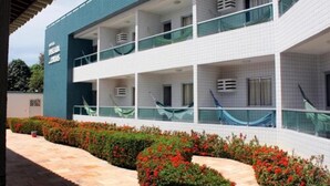 A two-story building with a tiled exterior, balconies with glass railings, and a landscaped garden with red flowers. - Hotel Enseada dos Corais (Cabo de Santo Agostinho)
