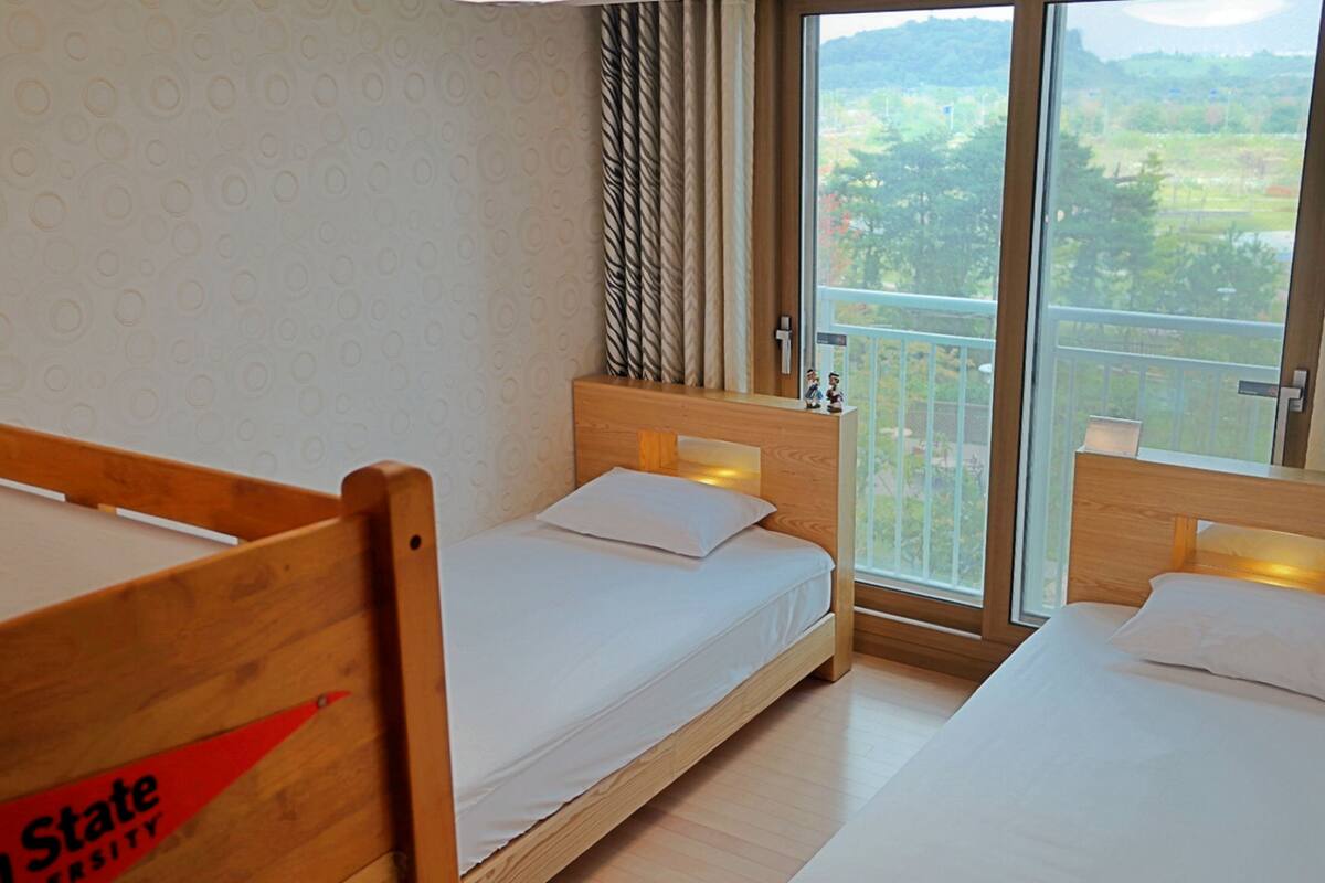 Habitació d'hotel amb dos llits de fusta, un finestral gran amb vista a vegetació i una paret amb un disseny decoratiu.