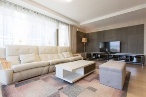 Uma sala de estar moderna com sofá, mesa de centro, banquinho e uma TV de tela plana na parede.