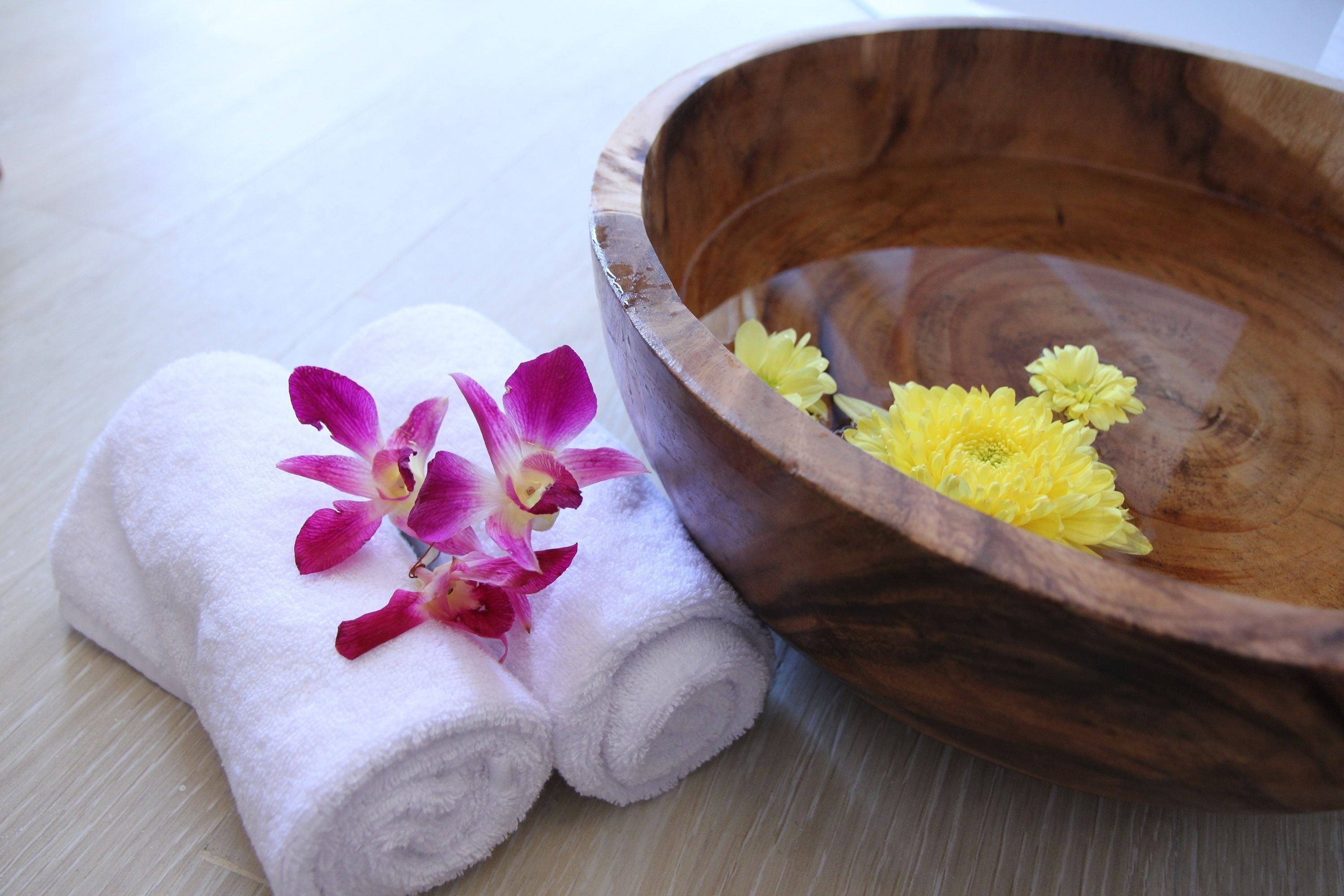 A wooden bowl with yellow flowers and rolled white towels with purple flowers.