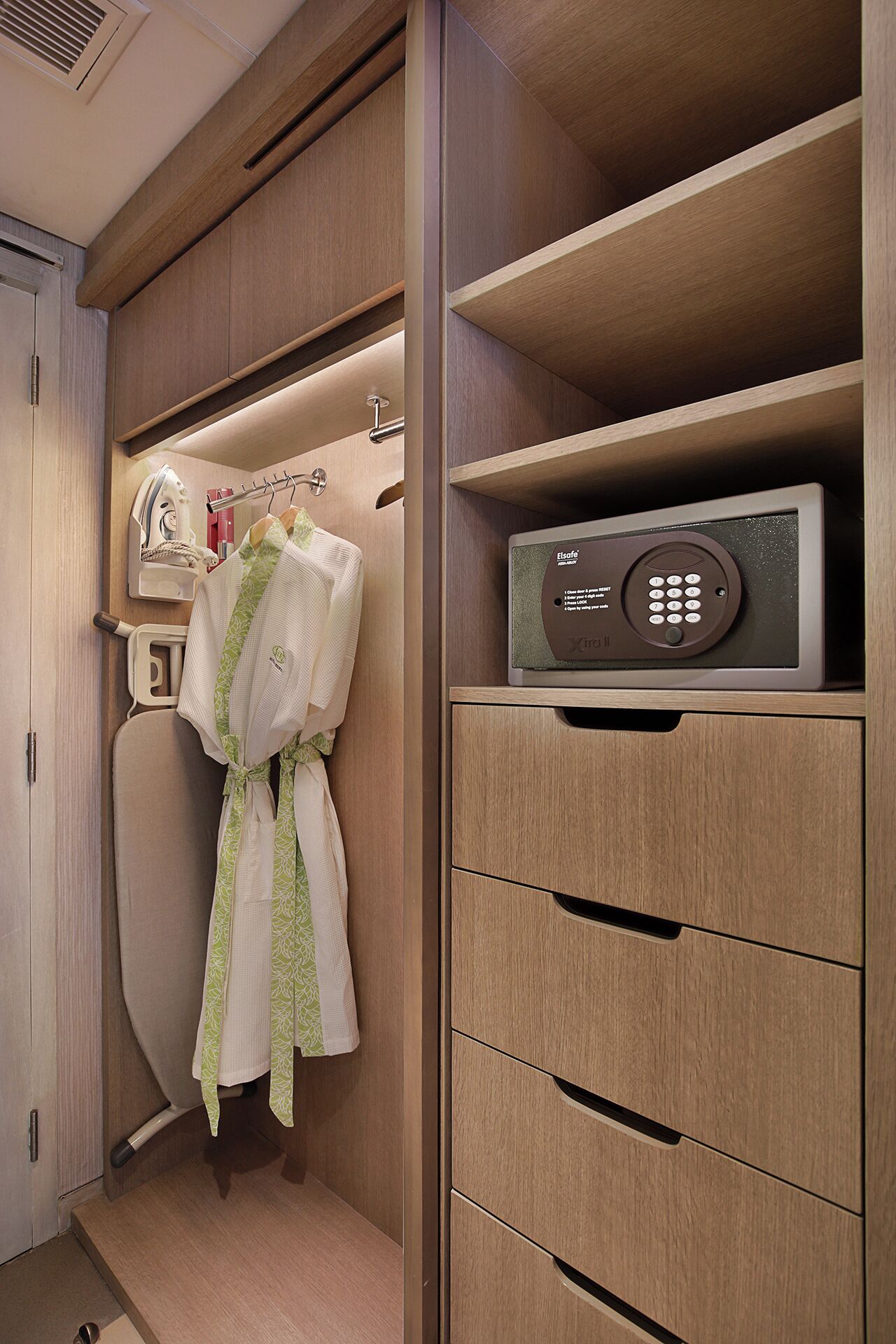 A compact, well-organized bathroom with a built-in ironing station, a towel rack, and a control panel for a water heater.