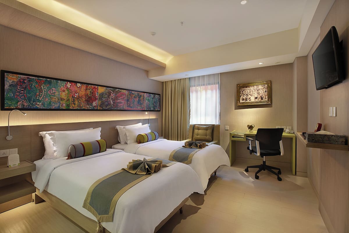 A hotel room with two beds, a desk, a chair, a television, and artwork on the walls.