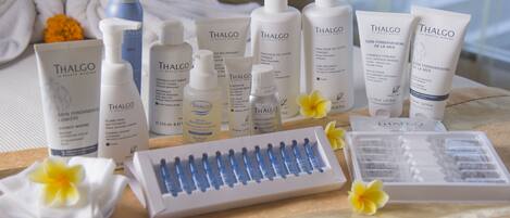 Variedad de productos de cuidado de la piel Thalgo dispuestos sobre una mesa con mantel blanco, junto a un pincel de maquillaje y una bandeja con cosméticos.