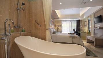 Un baño de hotel moderno con una bañera independiente, zona de ducha y una cama grande con vistas a la ciudad.