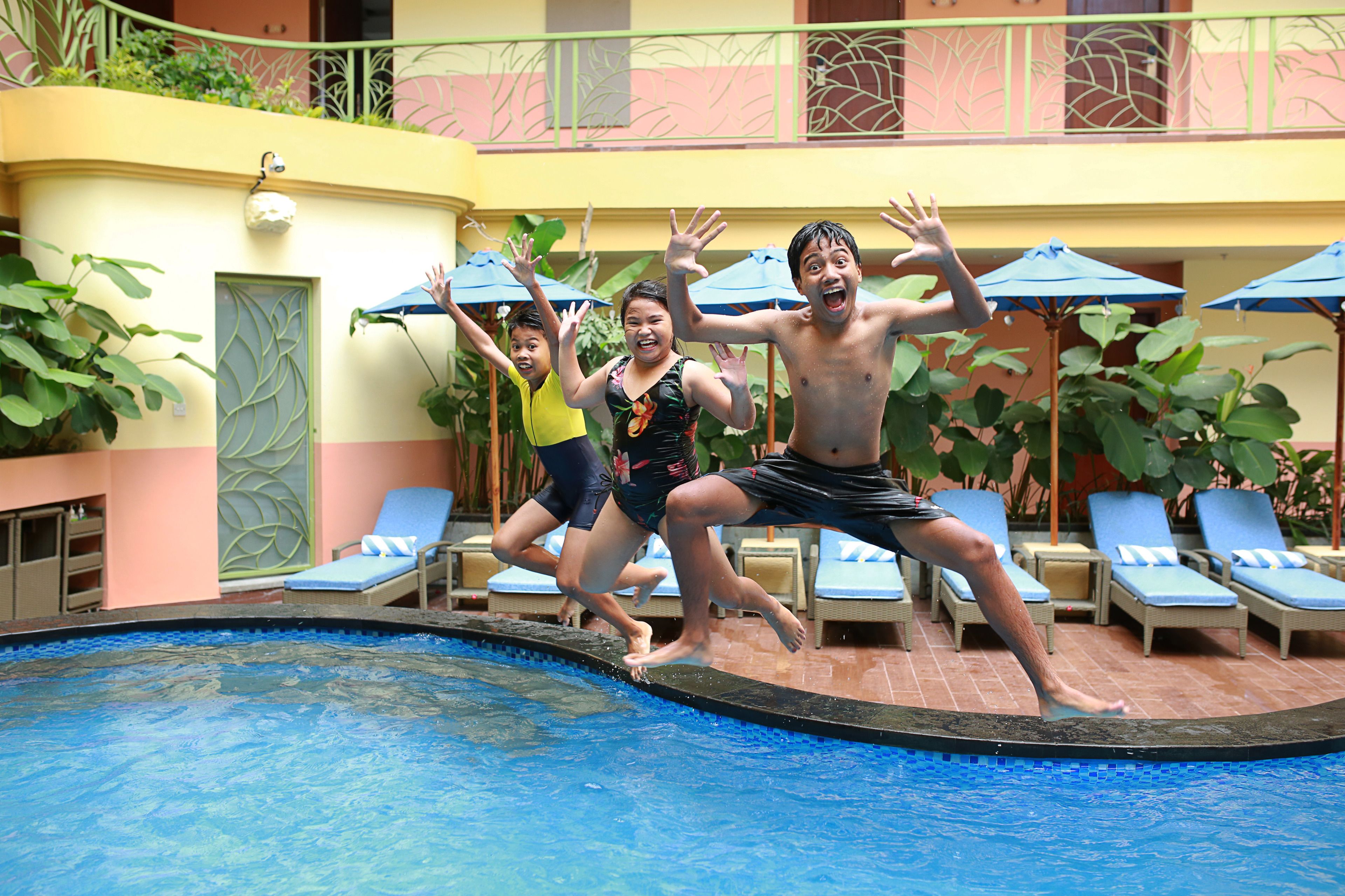 A swimming pool with lounge chairs and umbrellas, surrounded by a building with a balcony.