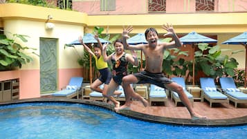A swimming pool with lounge chairs and umbrellas, surrounded by a building with a balcony.