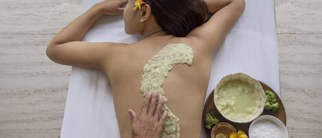 A person receiving a back treatment with a white towel and a tray of green paste and other items.