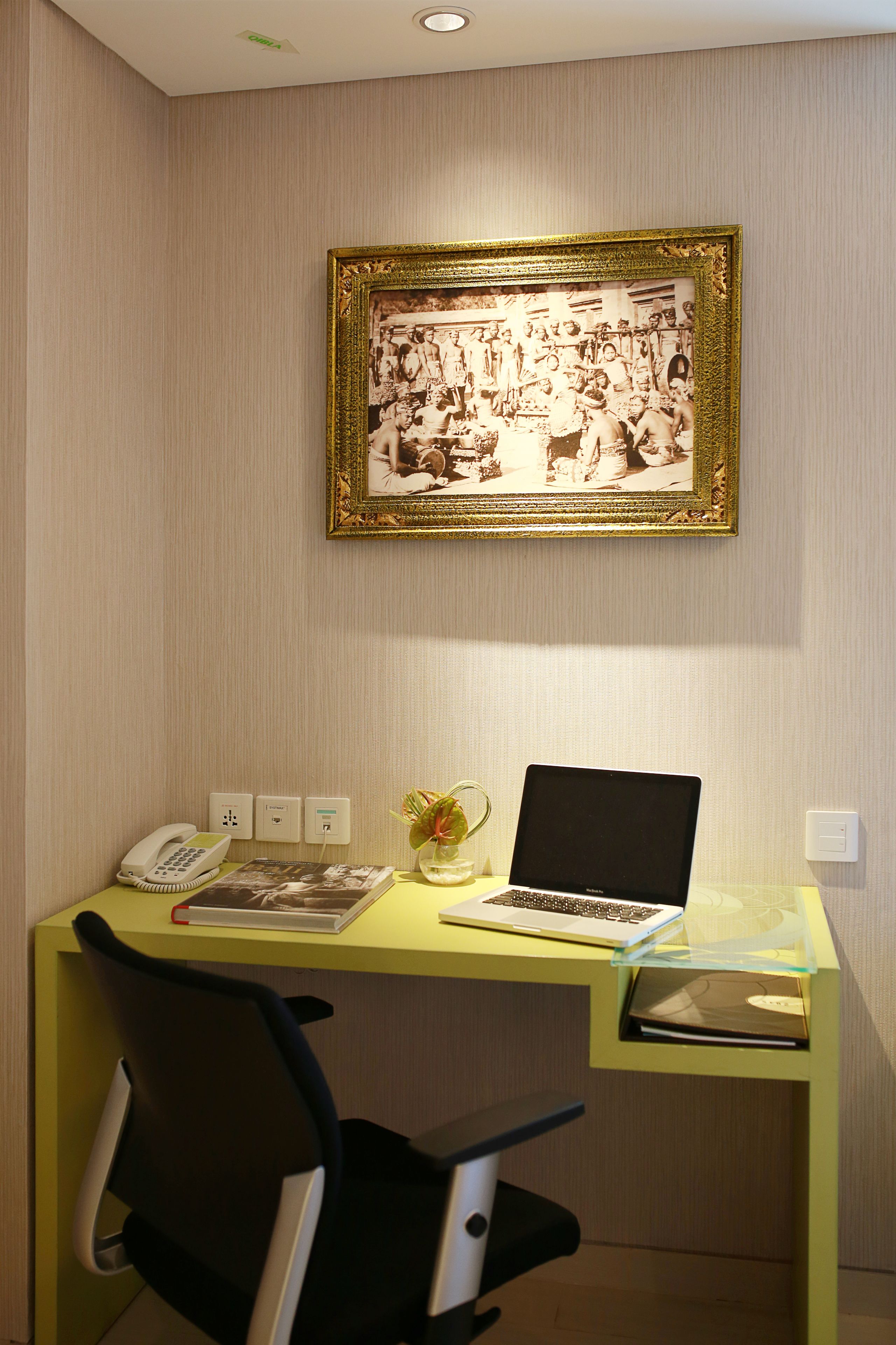 A desk with a laptop, a telephone, and a framed photograph on the wall.