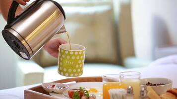 A person pouring coffee into a polka-dotted mug on a breakfast tray with eggs, toast, and a bowl of cereal.