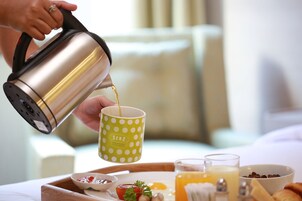 A person pouring coffee into a polka-dotted mug on a breakfast tray with eggs, toast, and a bowl of cereal.
