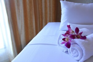 A neatly made bed with white linens, a rolled white towel, and purple orchids.