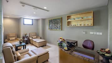 A reception area with a desk, chairs, a window, a painting, and shelves with items.