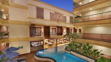 A multi-level hotel interior with a central swimming pool, multiple dining areas, and balconies with decorative railings.