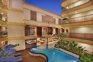 Interior de un hotel de varios niveles con una piscina central, varias zonas de comedor y balcones con barandillas decorativas.