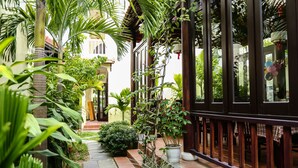 A narrow pathway flanked by lush greenery and a building with a dark wooden railing. - Hoi An Holiday Villa (Da Nang)