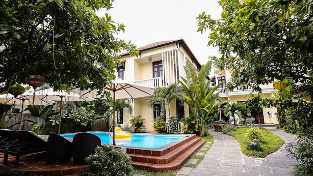 A pool area with lounge chairs, a pathway, and a building with a balcony. - Hoi An Holiday Villa (Da Nang)