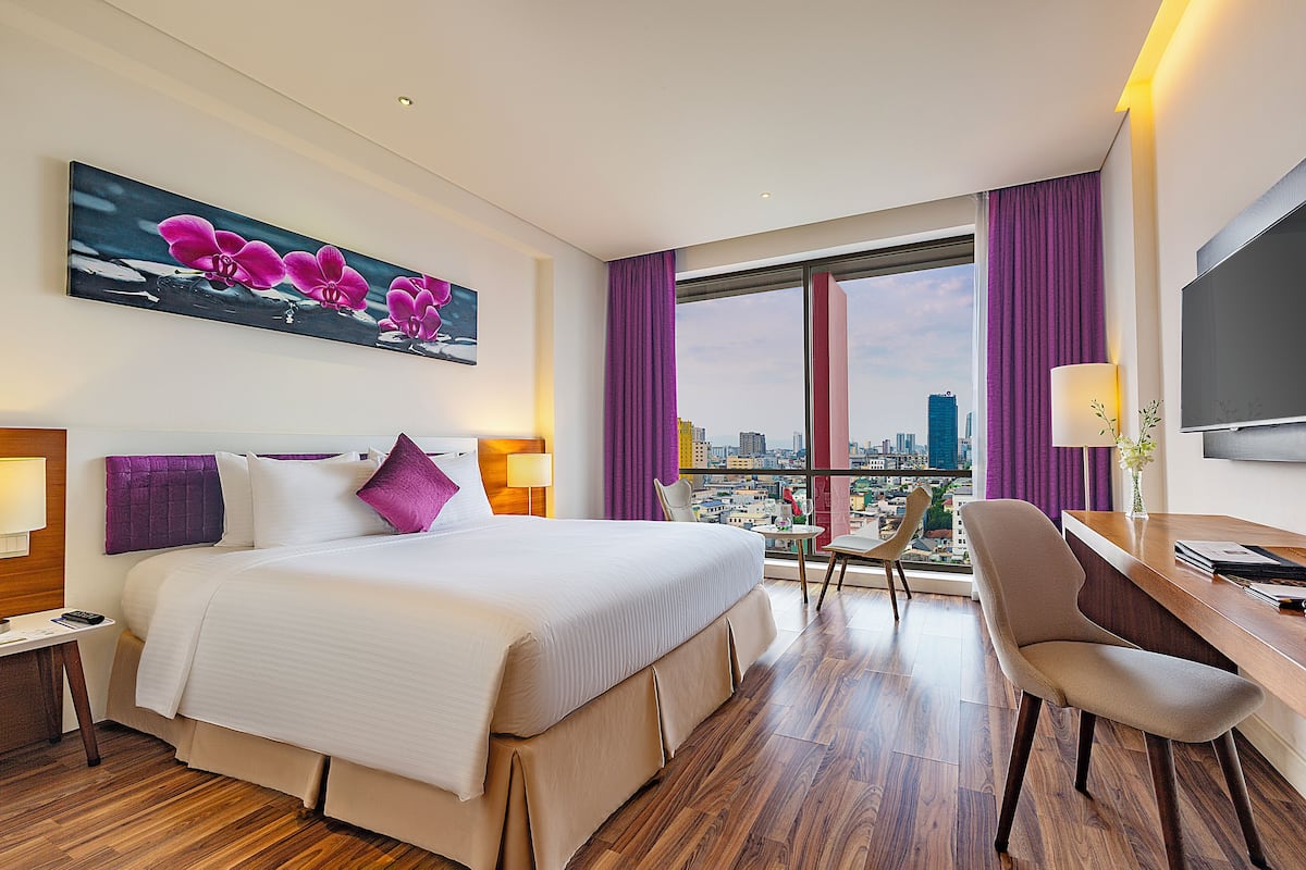 Habitación de hotel con una cama grande, un escritorio, una silla y vistas a la ciudad a través de la ventana.