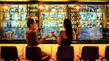 Zona de bar con un letrero del Vanda Hotel, estantes llenos de botellas de licor y dos personas sentadas en la barra.