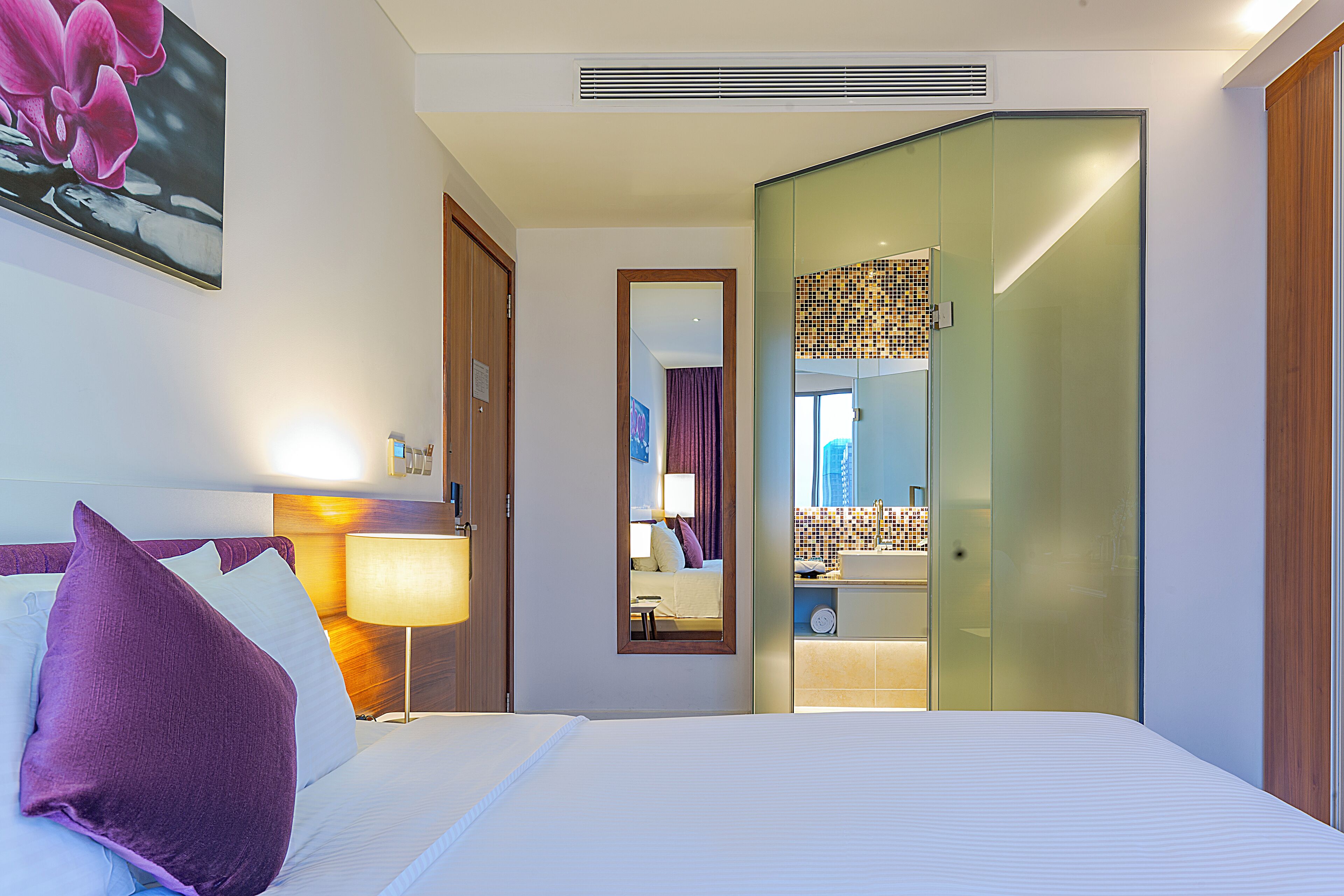 Una habitación de hotel con cama, mesita de noche, lámpara, espejo y armario.