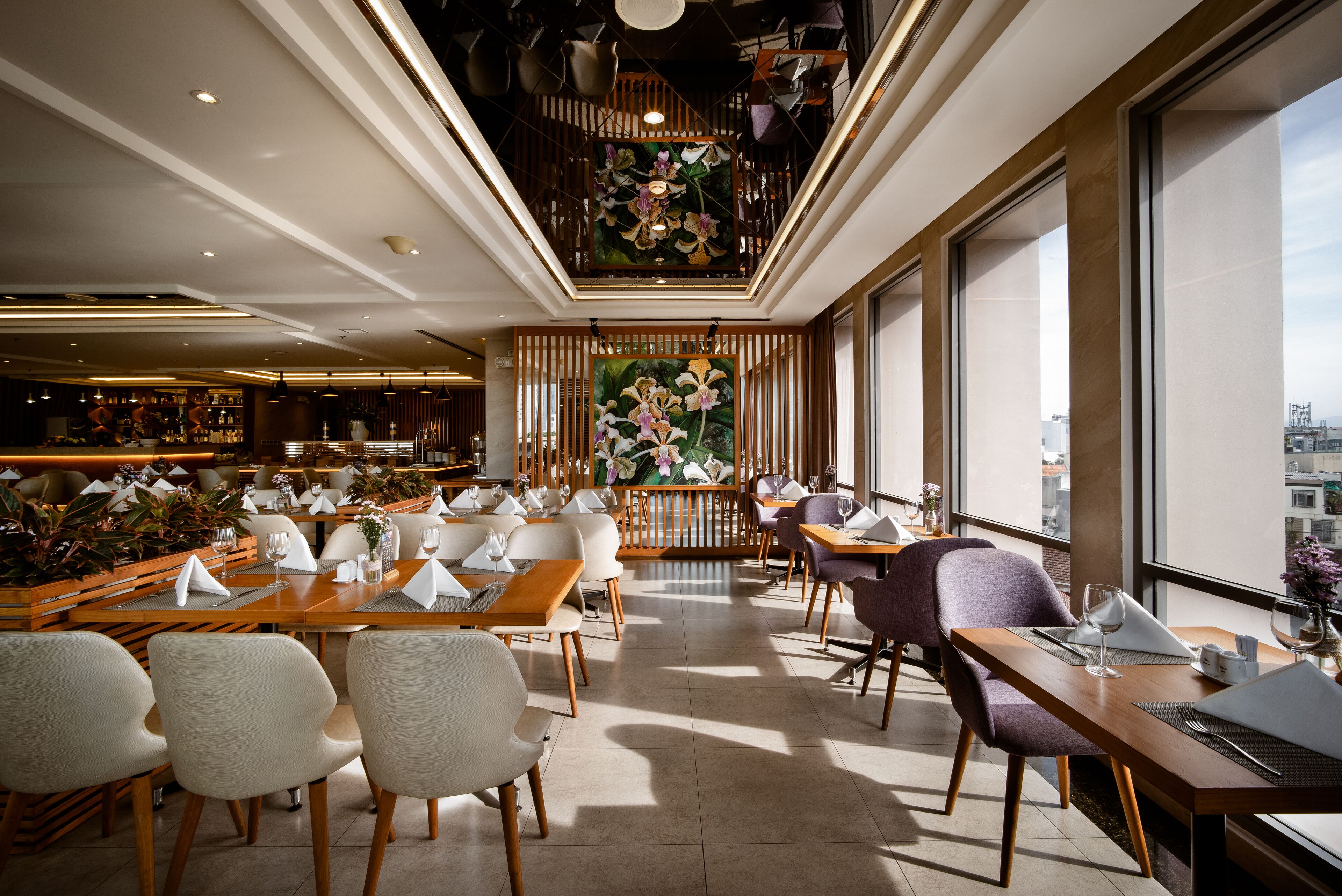 En moderne restaurant med træborde og stole, et stort blomsterbillede og udsigt over byen gennem store vinduer.