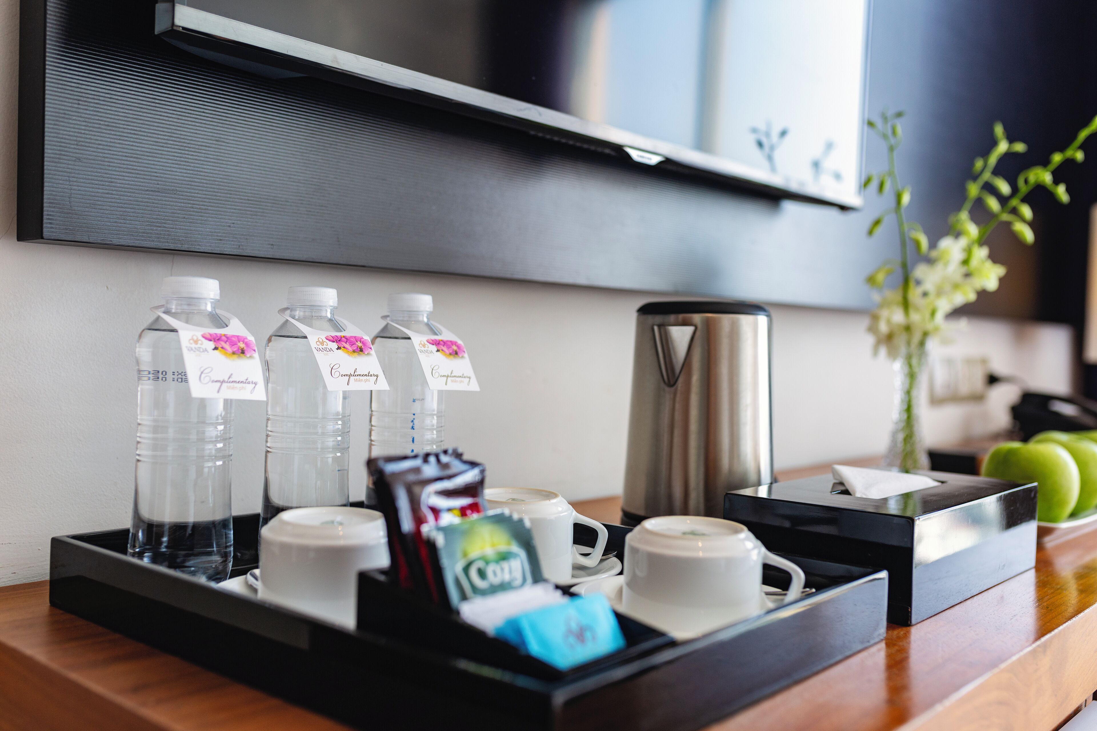 A breakfast tray with water bottles, coffee, tea, and a coffee maker on a wooden counter.