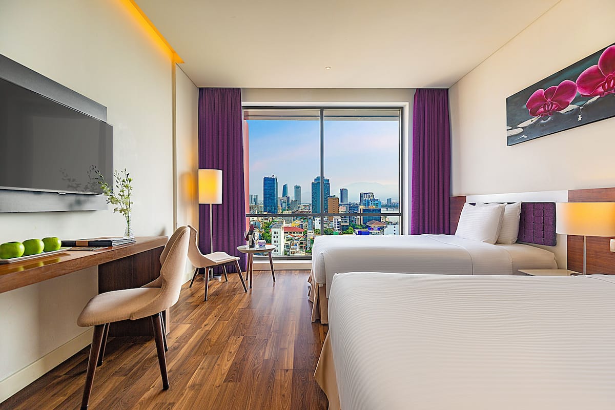 Habitación de hotel con vista a la ciudad, un escritorio con silla, dos camas y un televisor.