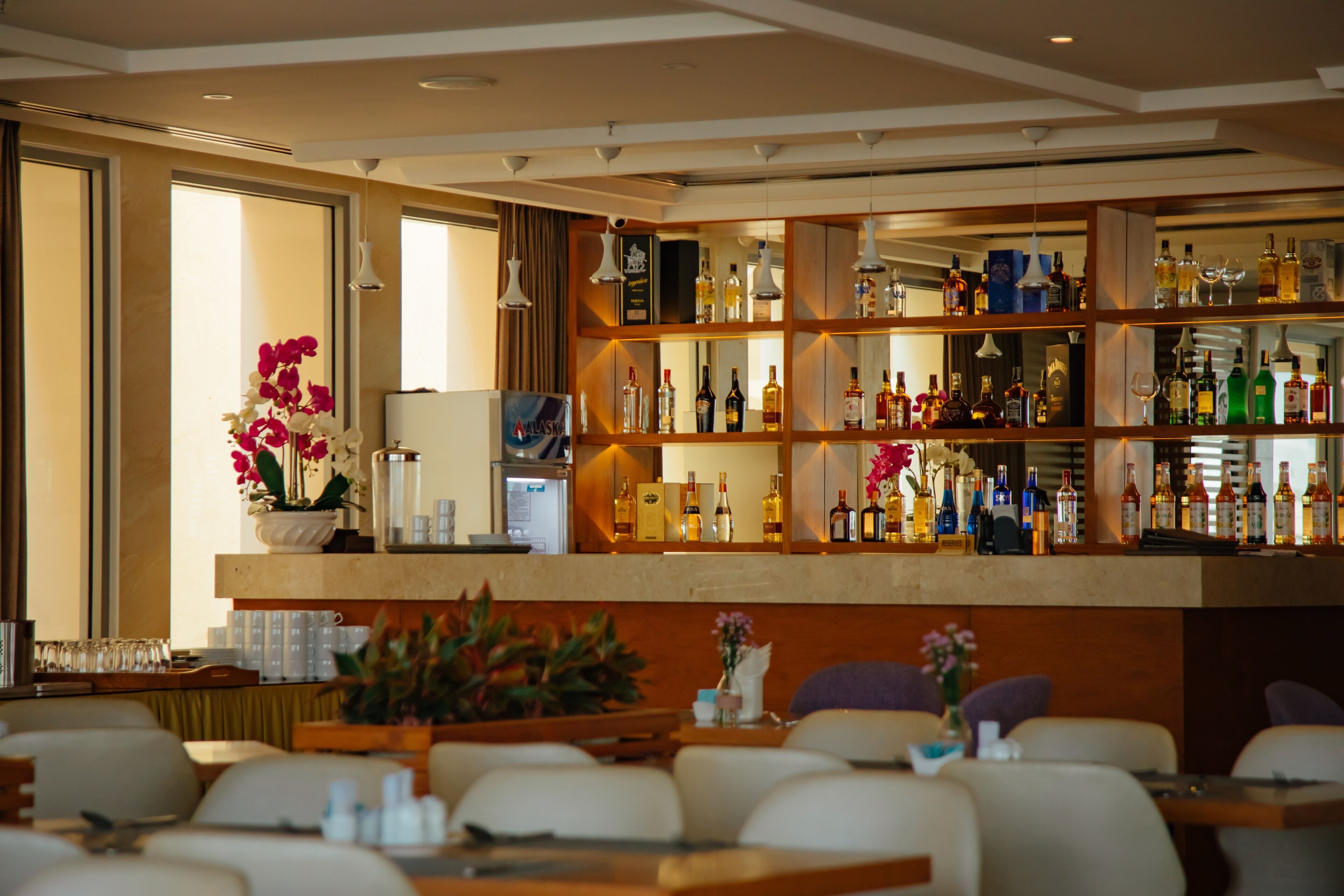 A bar area with shelves of liquor bottles, a coffee machine, and seating with tables.